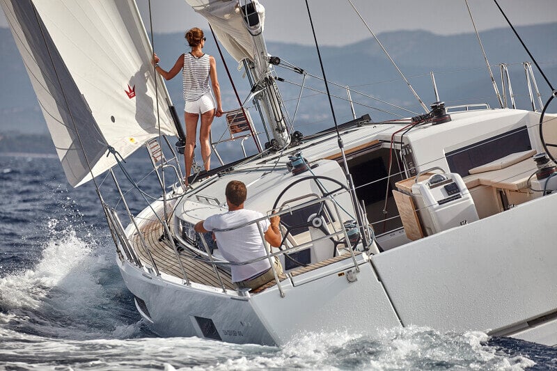 Sun Odyssey 490 - tyylikäs purjevene avomerellä, purjeet täysin nostettuna ja matkustajat nauttimassa purjehduksesta.